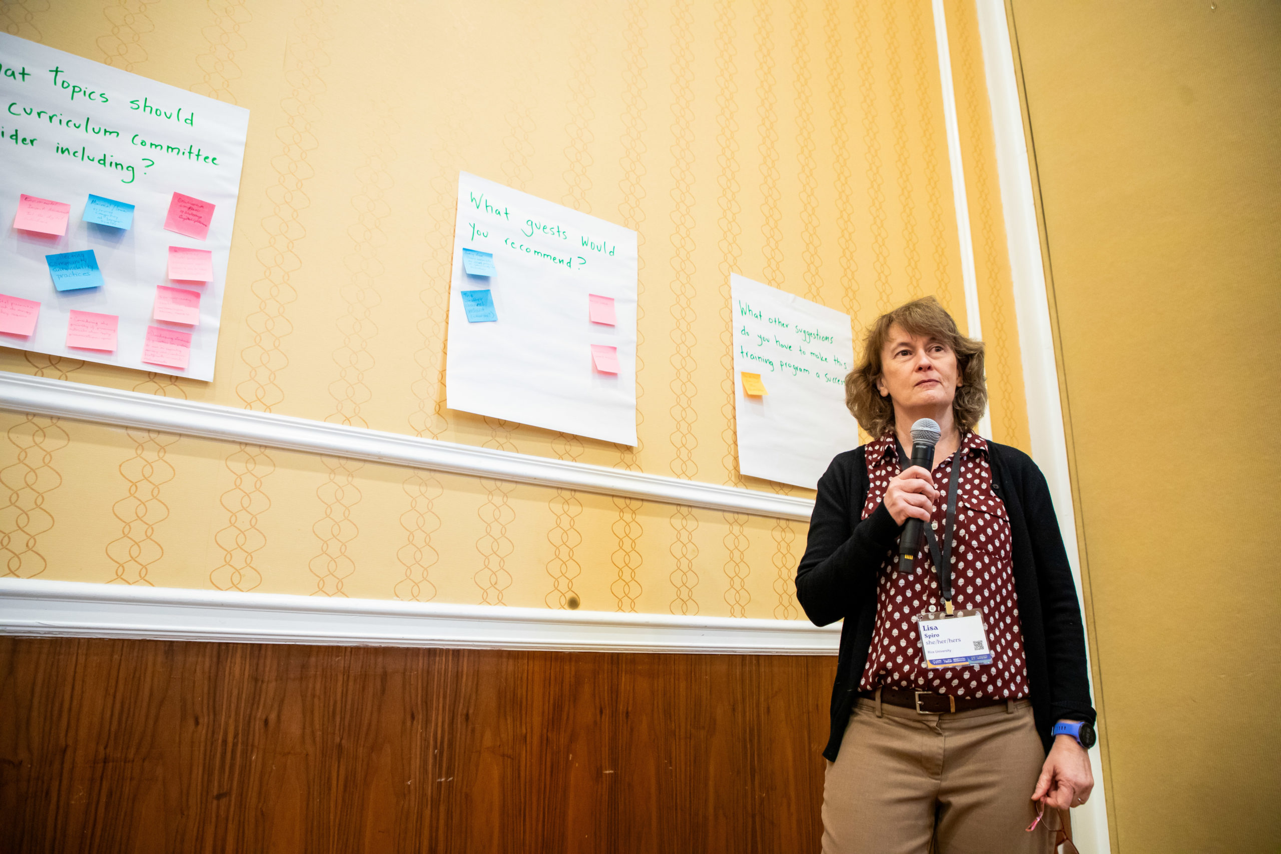 Person holding microphone in front of a wall with large sticky notes with smaller sticky notes on them.